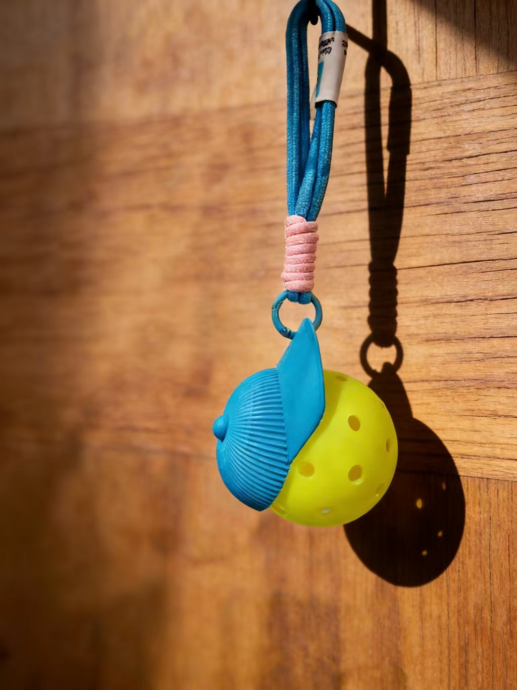 RallyWell blue pickleball cap keychain with ball hanging on wood background